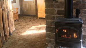 Un interior rústico con chimenea de piedra, vigas de madera y un ciervo montado en la pared.