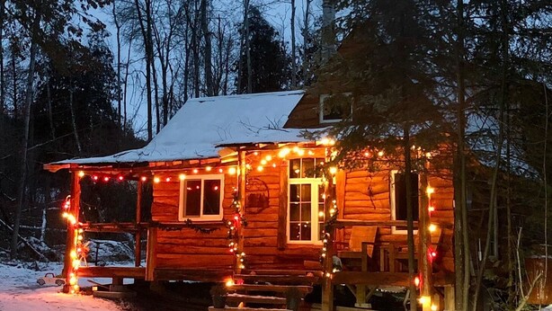 Una cabaña de madera con porche, rodeada de nieve y árboles.