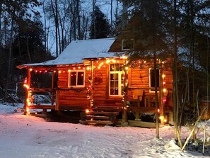 Una cabaña de madera con porche, rodeada de nieve y árboles.