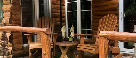 A log cabin with a patio area featuring wooden chairs, a table, and a black umbrella.