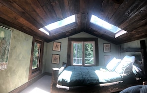 Un dormitorio acogedor en el ático con techo inclinado, tragaluces, una cama grande y cuadros enmarcados en las paredes.