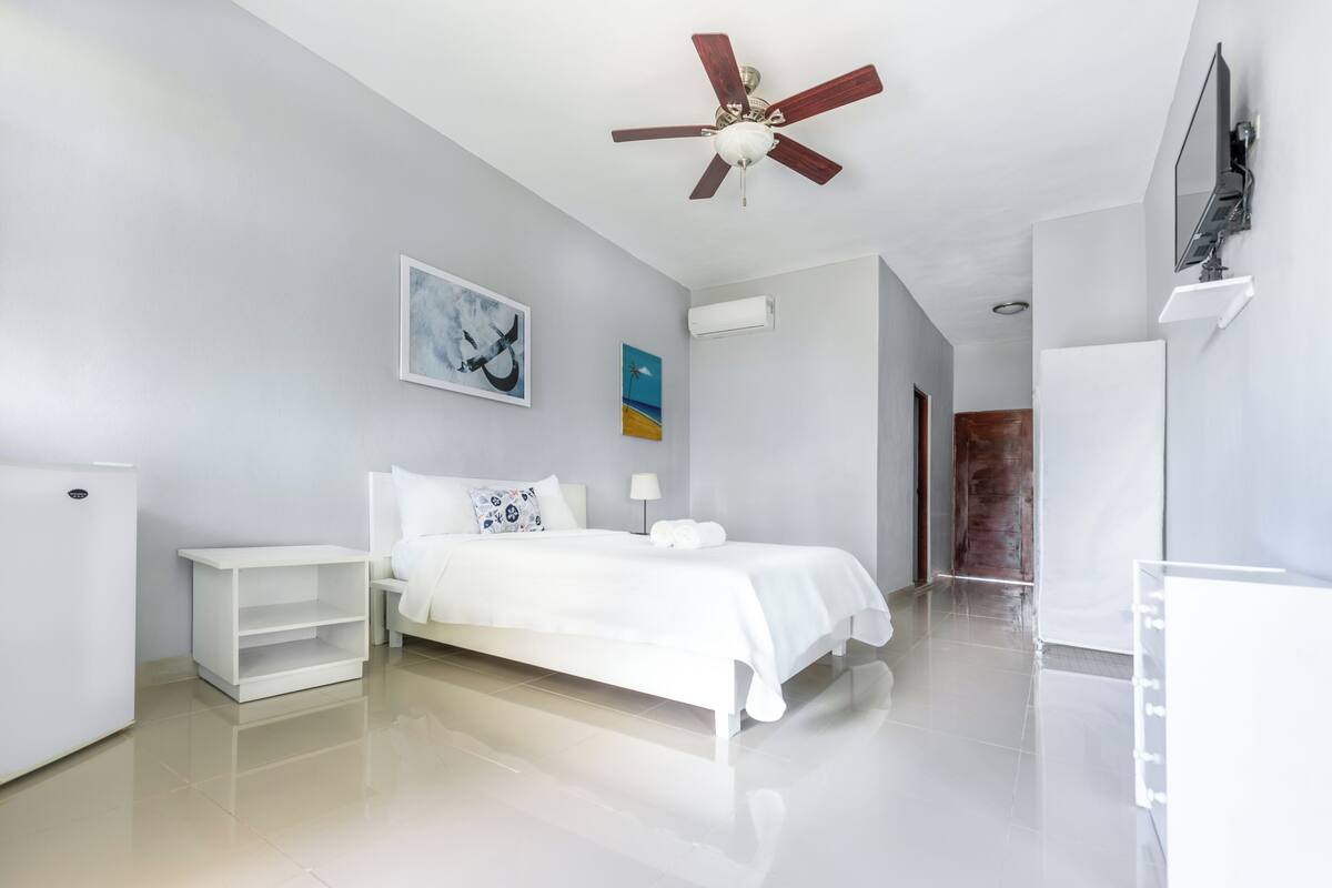 A modern hotel room with a bed, a nightstand, a ceiling fan, and artwork on the walls.