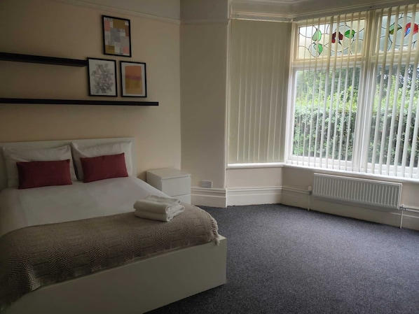 Habitación de hotel con cama, mesita de noche, radiador y ventana con persianas.