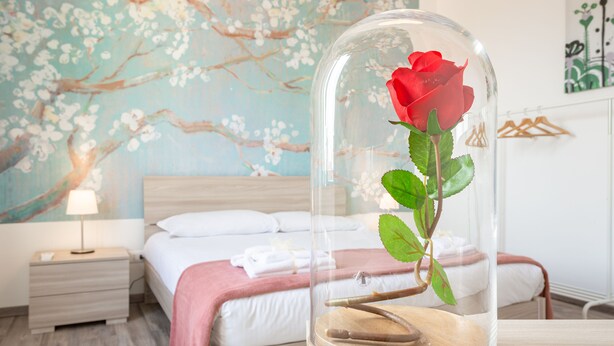 Camera da letto con un letto, un comodino e una cupola di vetro che contiene una rosa.