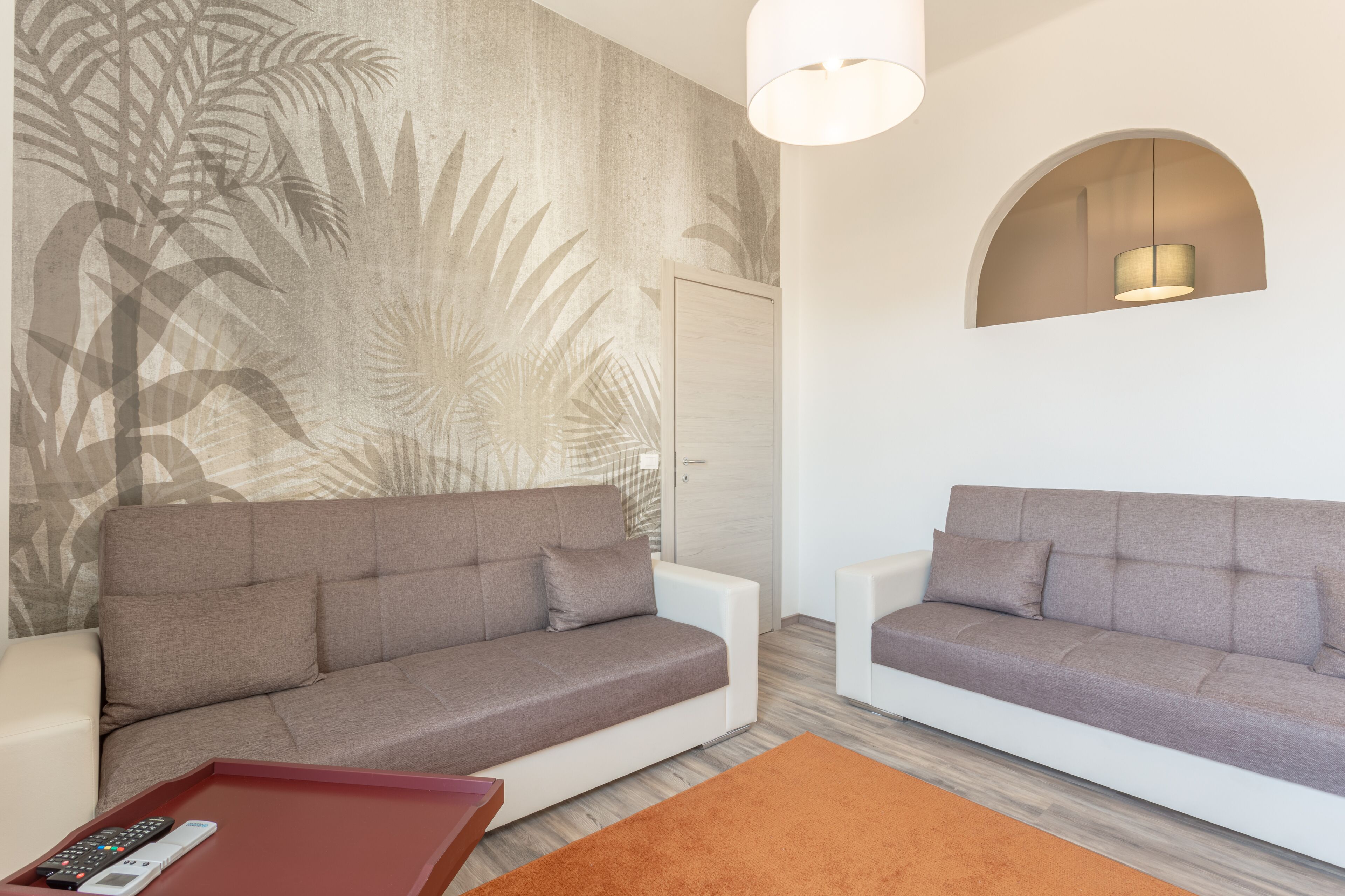 Un salon moderne avec deux canapés, une petite table basse rouge et une grande fresque murale.