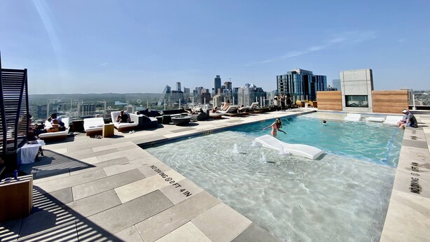 Ein Pool auf dem Dach mit klarem Wasser, umgeben von Liegestühlen und einer Skyline im Hintergrund.