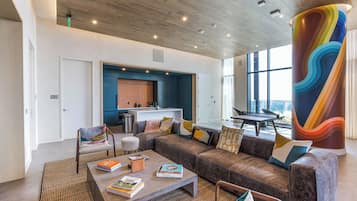 A modern living room with a sectional sofa, a coffee table with books, a large colorful pillar, and a view of the outdoors through large windows.