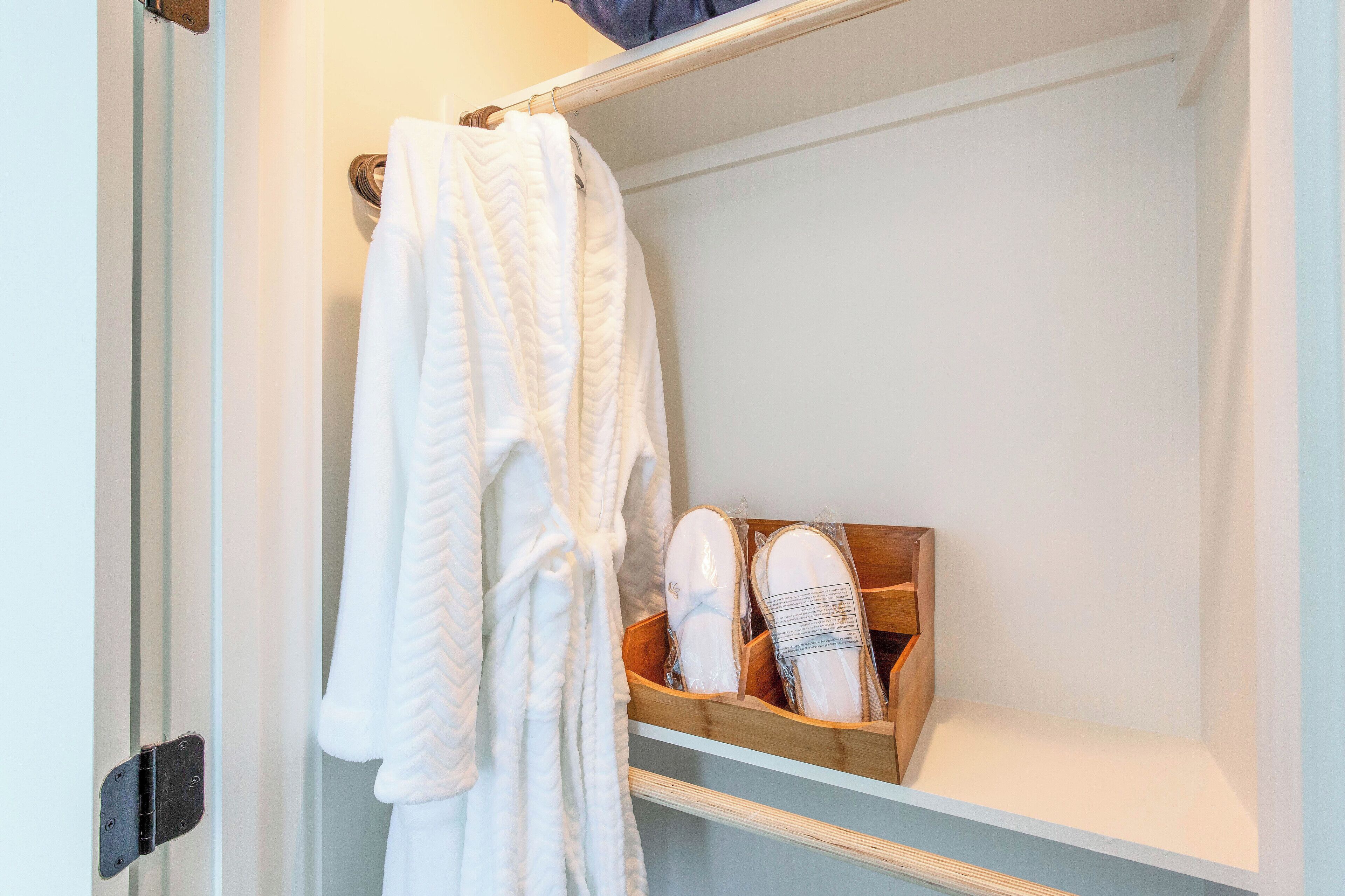 Un baño con un toallero blanco que sostiene dos toallas blancas, un zapatero de madera con zapatos, y un estante blanco.