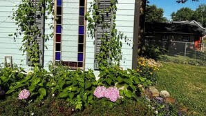 Une maison avec un jardin à l’avant, agrémentée d’une clôture en bois, d’un banc en bois et de diverses plantes et fleurs.