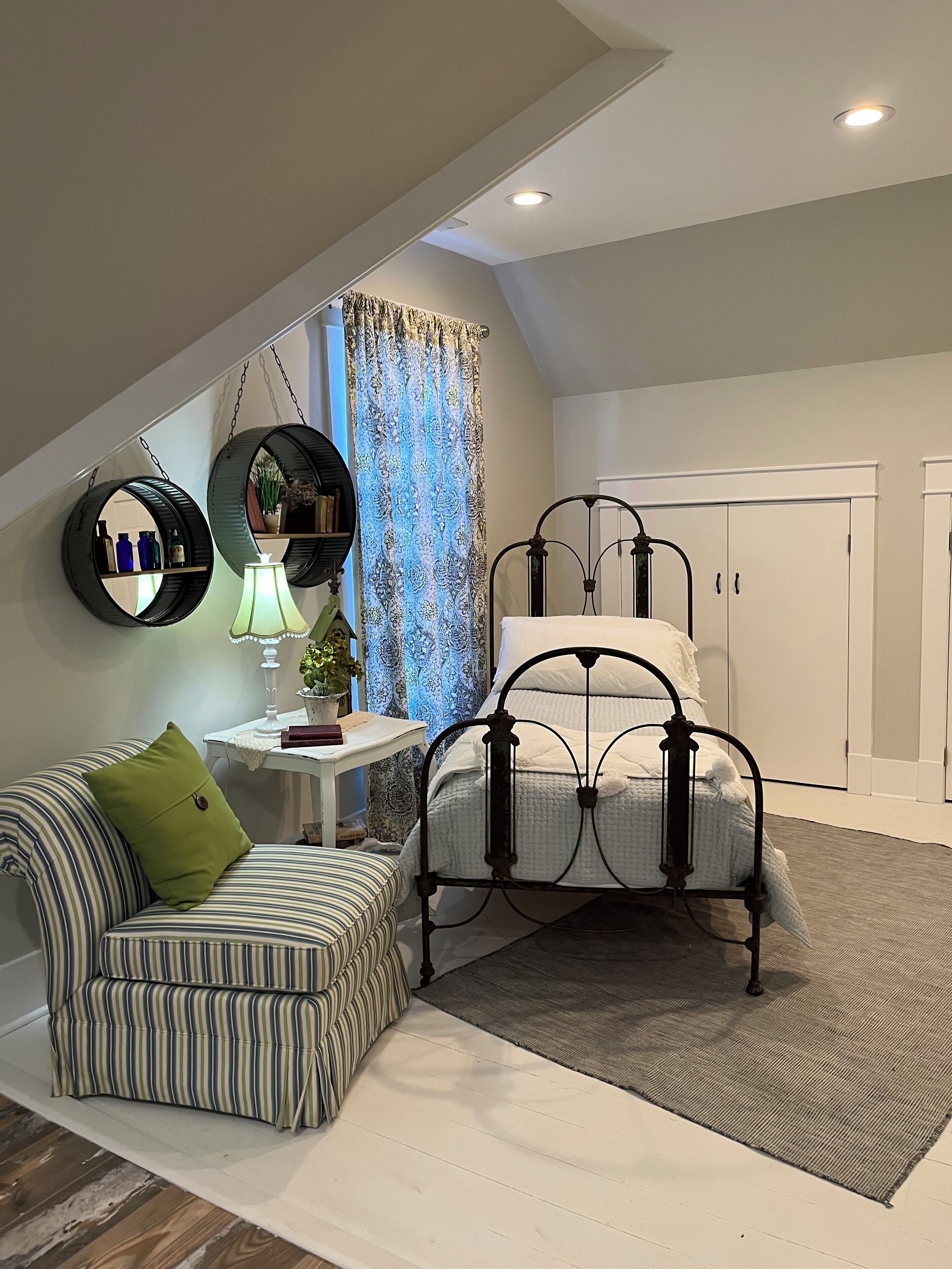 A bedroom with a bed, a chair, a small table, a lamp, and a wardrobe.