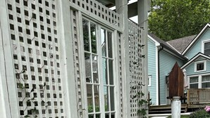 Une clôture en bois peinte en blanc, ornée d’un motif en treillis, une fenêtre et un jardin avec différentes espèces de plantes.