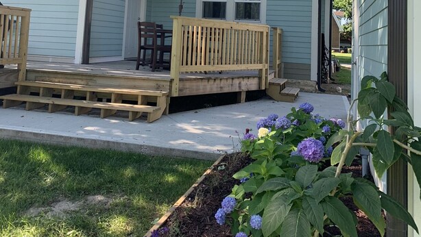 Une propriété résidentielle dotée d’un porche couvert, d’une terrasse en bois et d’un jardin agrémenté d’hortensias.