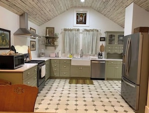 A kitchen with green cabinets, a stainless steel refrigerator, and a tiled floor. - Super Charming Modern Cottage (Pendleton)