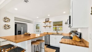 Una cocina moderna con una isla de madera, taburetes de bar, lavavajillas, refrigerador y tostadora.