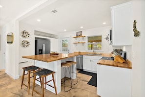A modern kitchen with a wooden island, bar stools, a refrigerator, and a dishwasher.