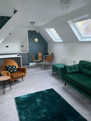 A modern loft apartment with a high ceiling, skylights, a green sofa, a wooden chair, and a small table.