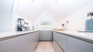 A modern kitchen with grey cabinets, a built-in oven, a microwave, and a coffee machine. There is a window providing natural light. - Luxury 3-bed Penthouse Apartment in Bournemouth (Bournemouth)