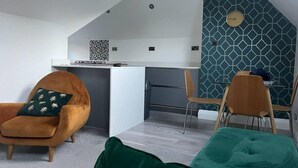 A modern kitchen with a geometric backsplash and a clock. There are two wooden chairs and a green sofa in a living area. - Luxury 3-bed Penthouse Apartment in Bournemouth (Bournemouth)