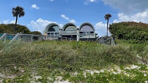 A beachfront property with three large arched structures, a palm tree, and a well-maintained lawn.
