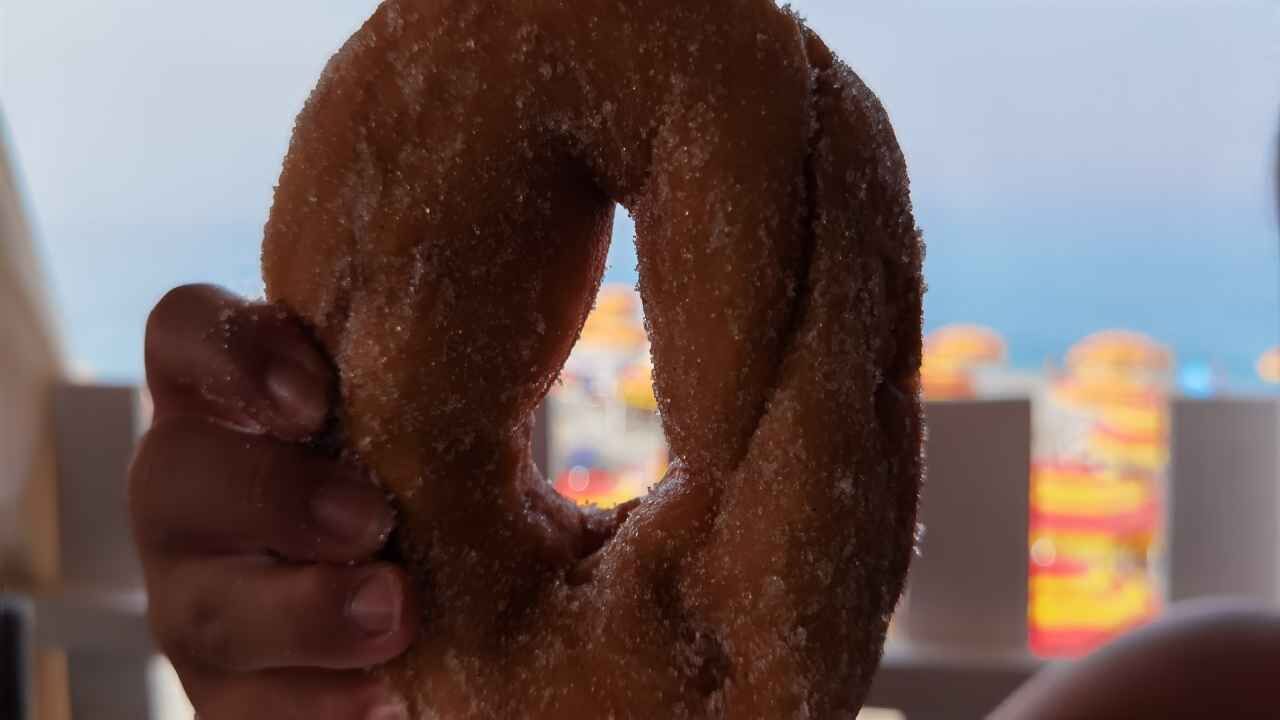 Uma mão segurando um donut com um buraco no centro.