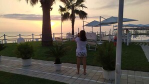 Una persona fotografiando la puesta de sol en una playa con palmeras, sillas de descanso y sombrillas.