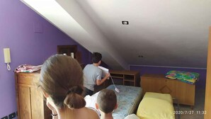 Una habitación con paredes moradas, un escritorio de madera, una cama con un almohadón amarillo y un niño jugando con un juguete.