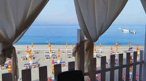 Vista sulla spiaggia con file di sedie a sdraio e ombrelloni, una ringhiera e il mare sullo sfondo.