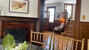 A dining area with a glass table, chairs, a fireplace, and a staircase leading to another room. - Eddie Manor: 1907 Gem in Downtown Meaford (Meaford)