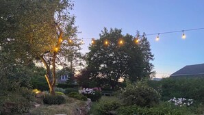 A garden with a stone pathway, a wooden deck, and string lights. - Eddie Manor: 1907 Gem in Downtown Meaford (Meaford)