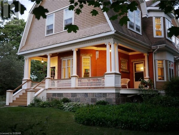 A two-story house with a front porch, a staircase leading to the entrance, and a well-maintained garden. - Eddie Manor: 1907 Gem in Downtown Meaford (Meaford)