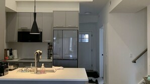 Een moderne keuken met een centraal eiland, barkrukken, een hanglamp en uitzicht op de aangrenzende woonkamer.