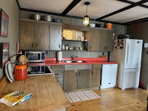 A compact kitchen with wooden cabinets, a red countertop, a microwave, a sink, and a refrigerator.