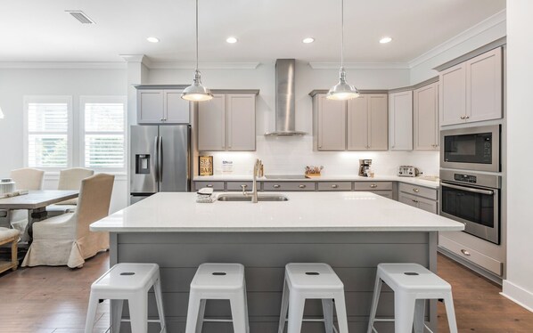 A modern kitchen with a large island, stainless steel appliances, and pendant lighting.