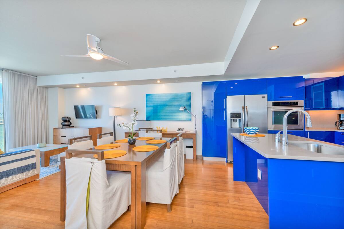 A modern kitchen with blue cabinets, a central island with a sink, and a dining area with a table and chairs.