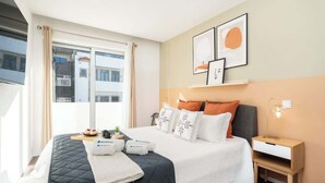 Una habitación de hotel moderna con una cama grande, una mesita de noche y un ventanal con cortinas.
