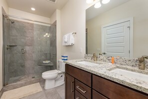 Une salle de bain moderne avec une douche à parois de verre, des toilettes blanches, un lavabo en marbre et un grand miroir.