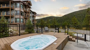 A wooden deck with a hot tub, a fenced area, and a view of a mountain and forest. - Brand New Luxury Condo/Mountain Views/Shared Hot Tub (Keystone)