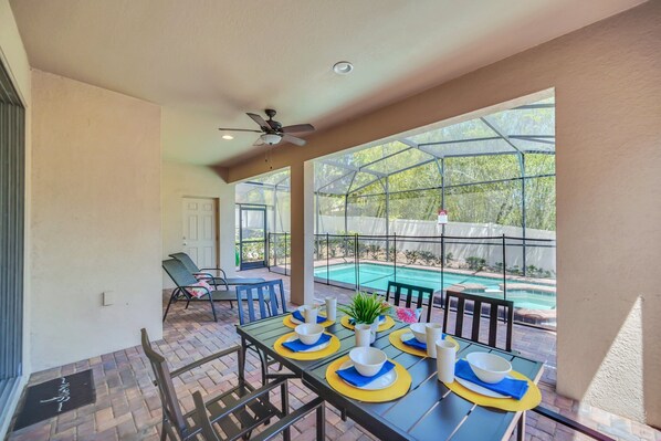 A patio area with a table set for dining, a ceiling fan, and a view of a swimming pool.