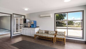A room with a kitchenette, a sofa, and large windows.