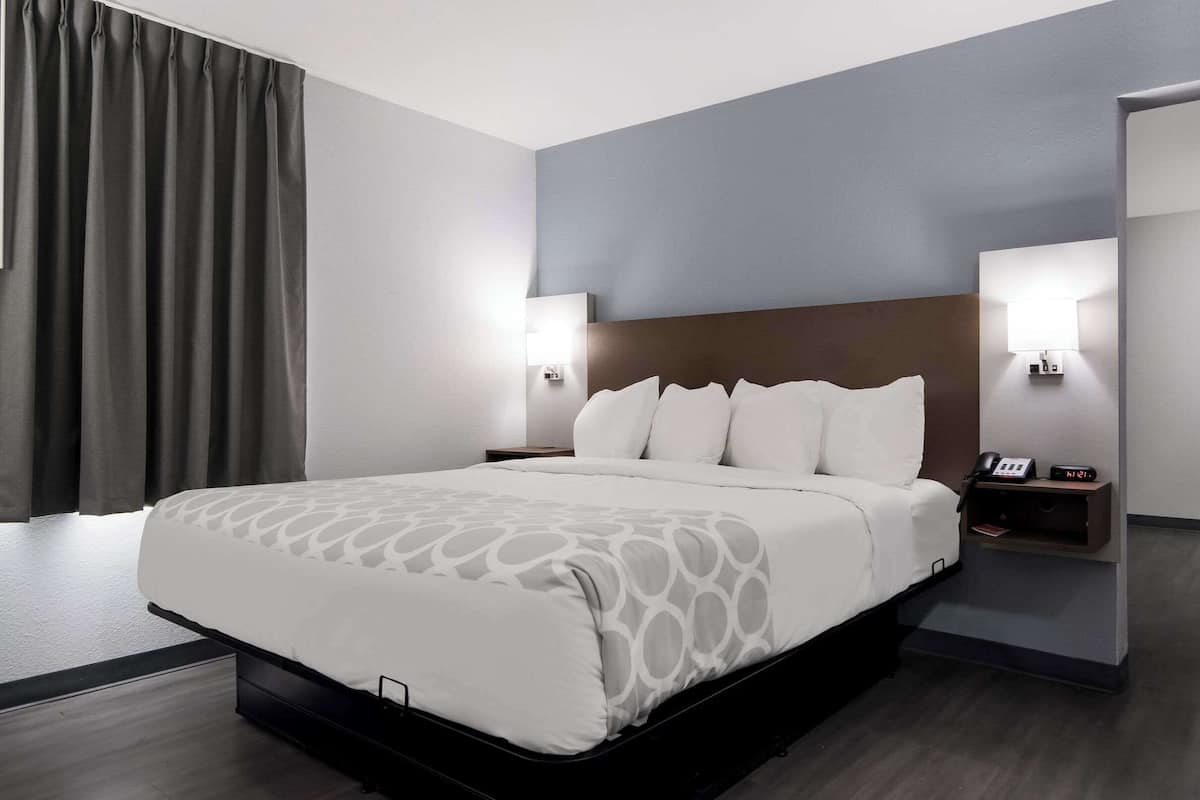 A modern hotel room with a large bed, bedside tables with lamps, and a view of the hallway.