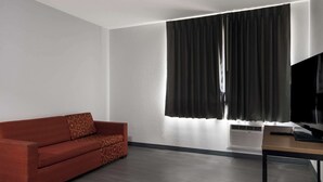 A modern room with a sofa, a television, and a window with curtains.