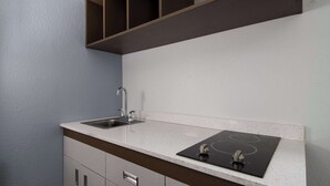 A kitchen with a stainless steel sink, a black stovetop, and a white countertop.