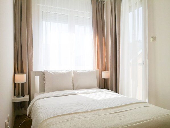 A hotel room with a bed, two bedside lamps, and sheer curtains.