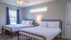 Un dormitorio con dos camas, un ventilador de techo, una ventana con cortinas y una mesita de noche con una lámpara.