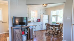 Una cocina con armarios de madera, un televisor, una cafetera y un comedor con sillas.