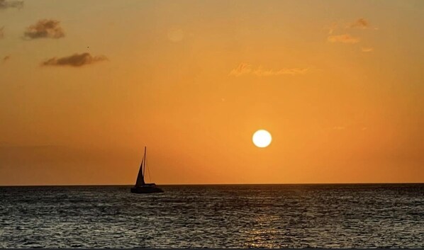 A sunset over the ocean with a sailboat. - Aruba Local Private House (Aruba)