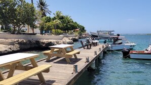 Eine Holzsteg erstreckt sich ins klare, blaue Wasser, mit Picknicktischen und dort anliegenden Booten.