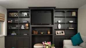 Una sala de estar moderna con muebles de madera oscura, un televisor de pantalla plana y un sofá gris con cojines turquesa.