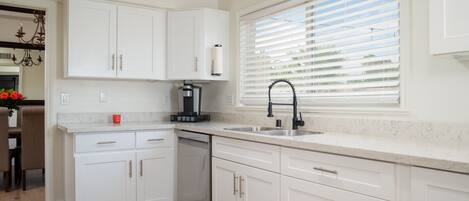 Una cocina moderna con armarios blancos, lavavajillas integrado y ventana con persianas.