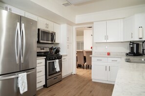 Una cocina moderna con electrodomésticos de acero inoxidable, armarios blancos y piso de madera.